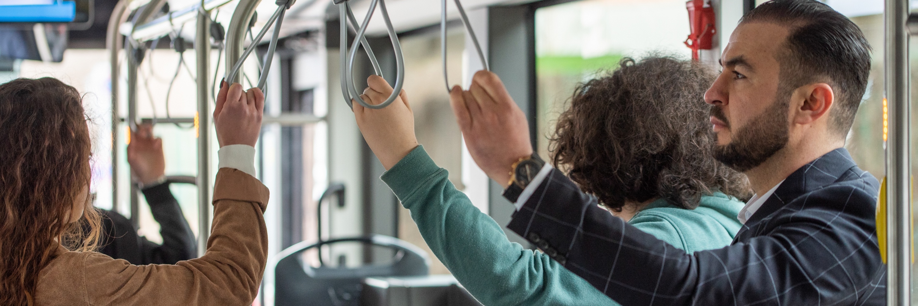 Tre passeggeri in piedi in autobus si sorreggono ai sostegni.